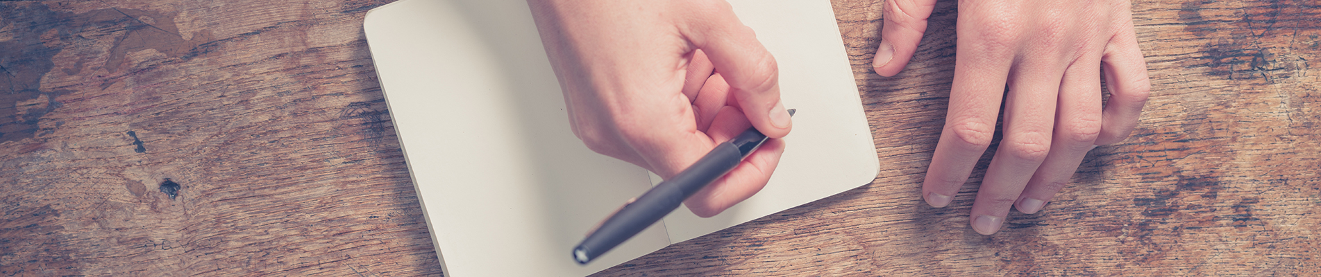 Woman writing in notepad at wooden table